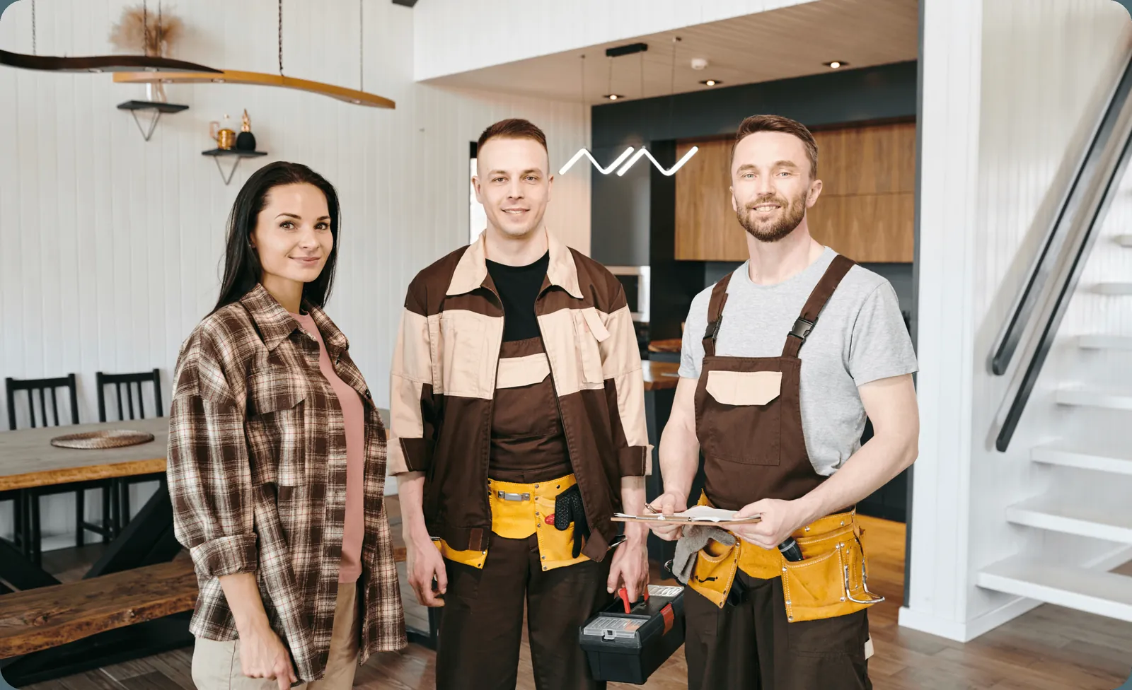 Three smiling renovation workers in tool belts in a finished kitchen