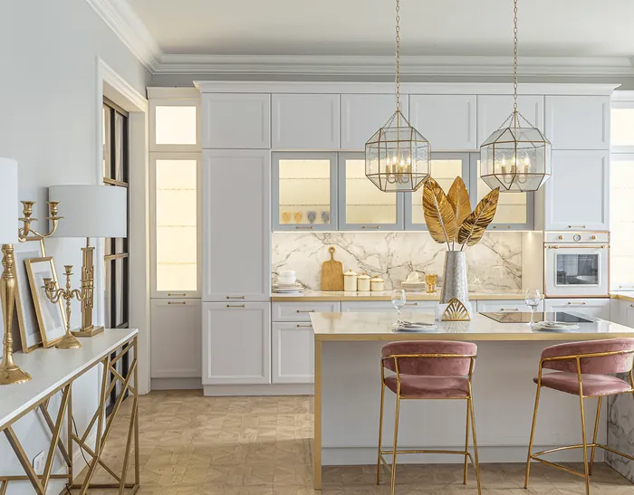 A white kitchen with glass pendants and pink velvet stools
