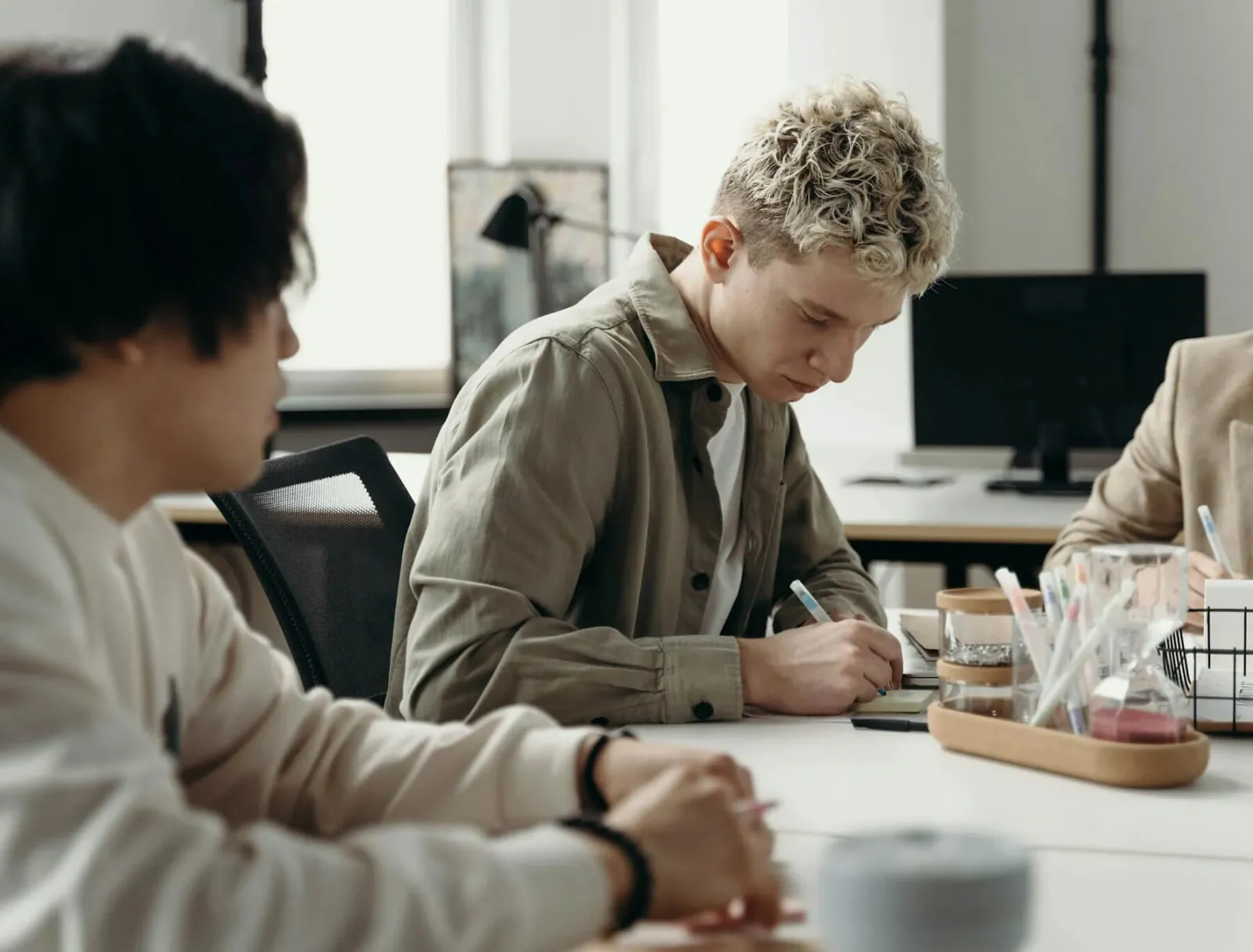 A man writing at a desk beside colleagues