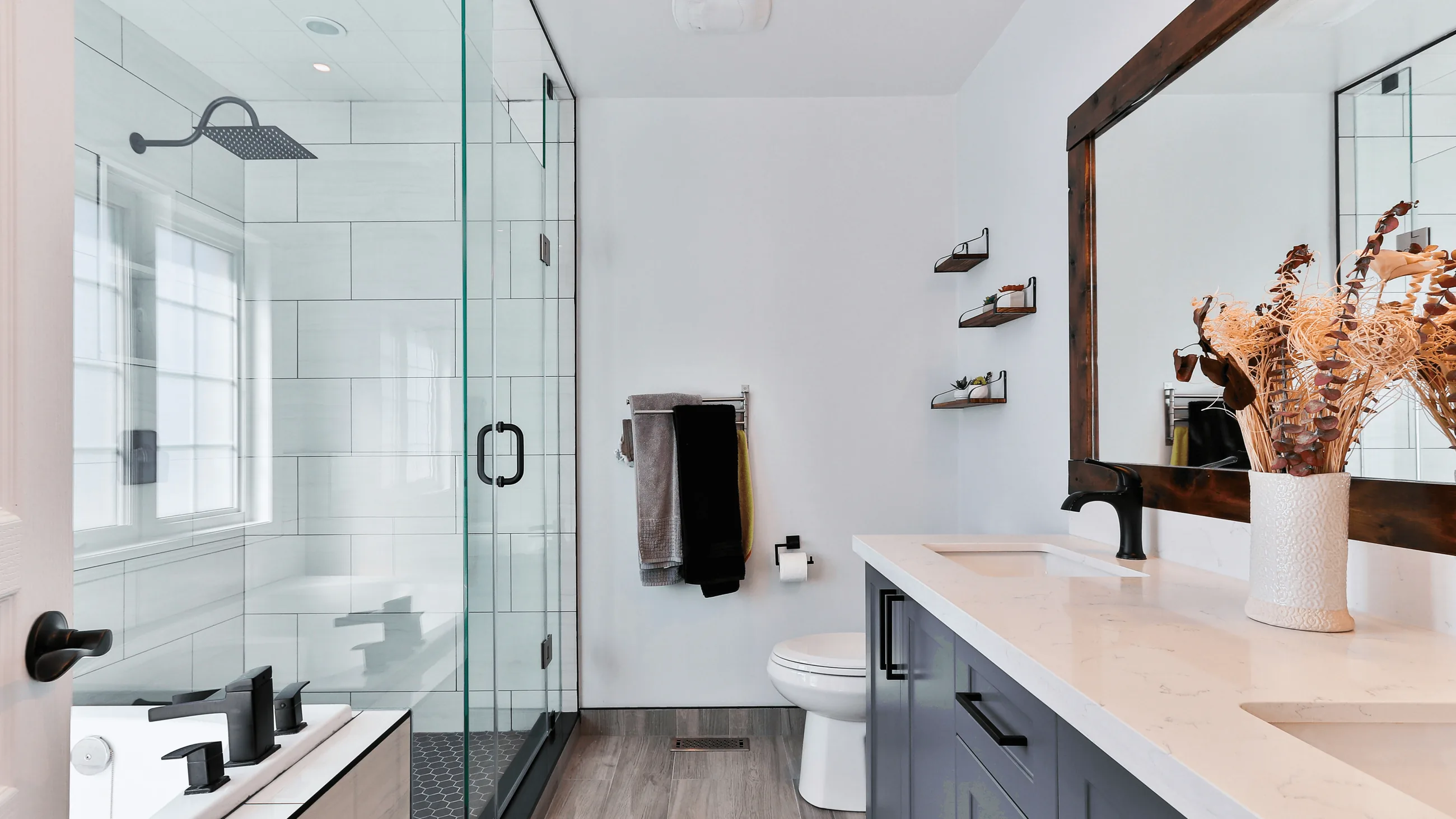 A bright bathroom with a glass shower and a wooden mirror