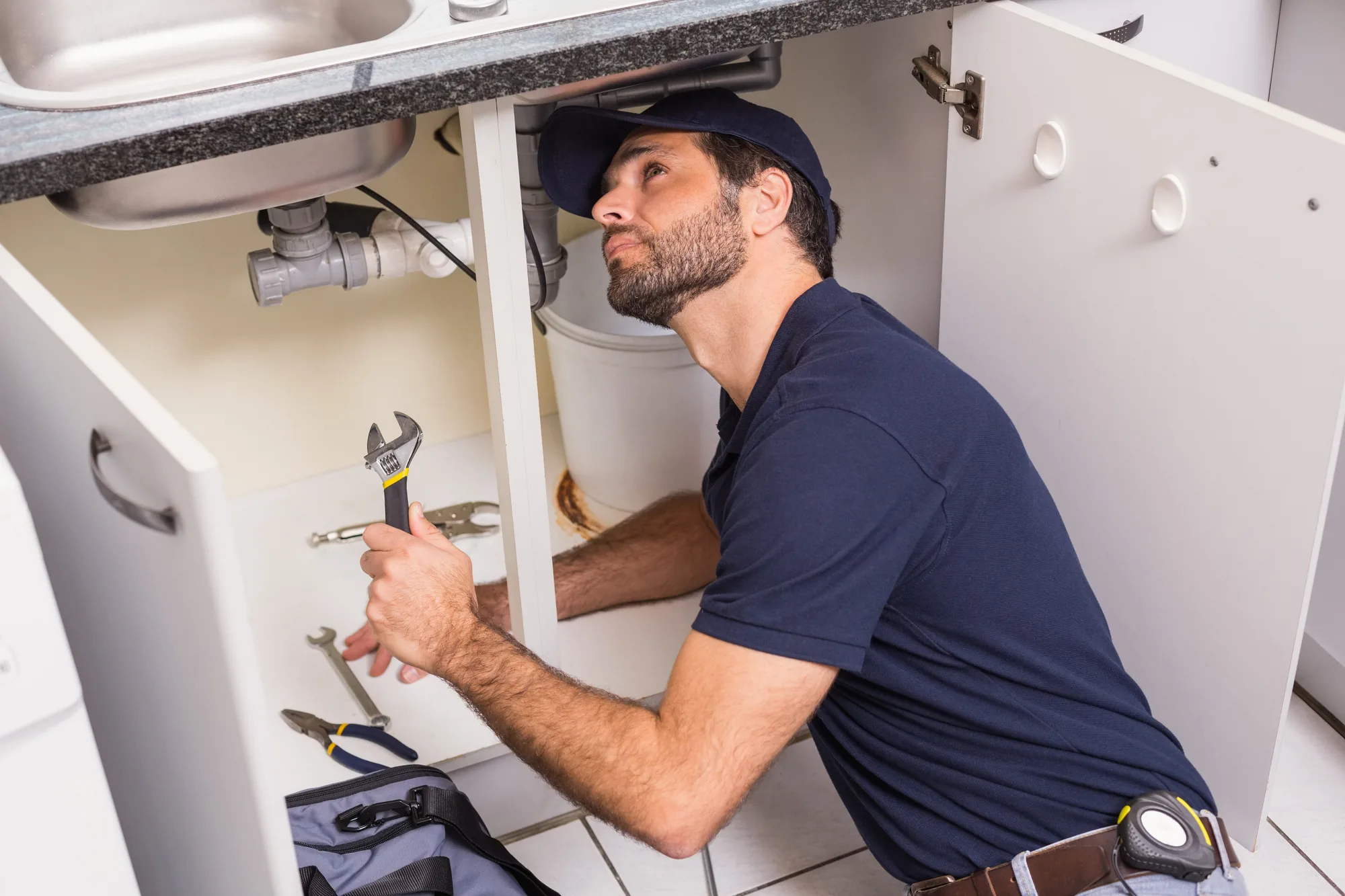 A plumber at work under a kitchen sink