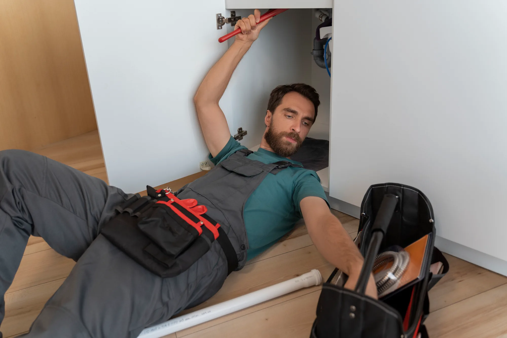 A plumber lying under a sink beside his tool bag