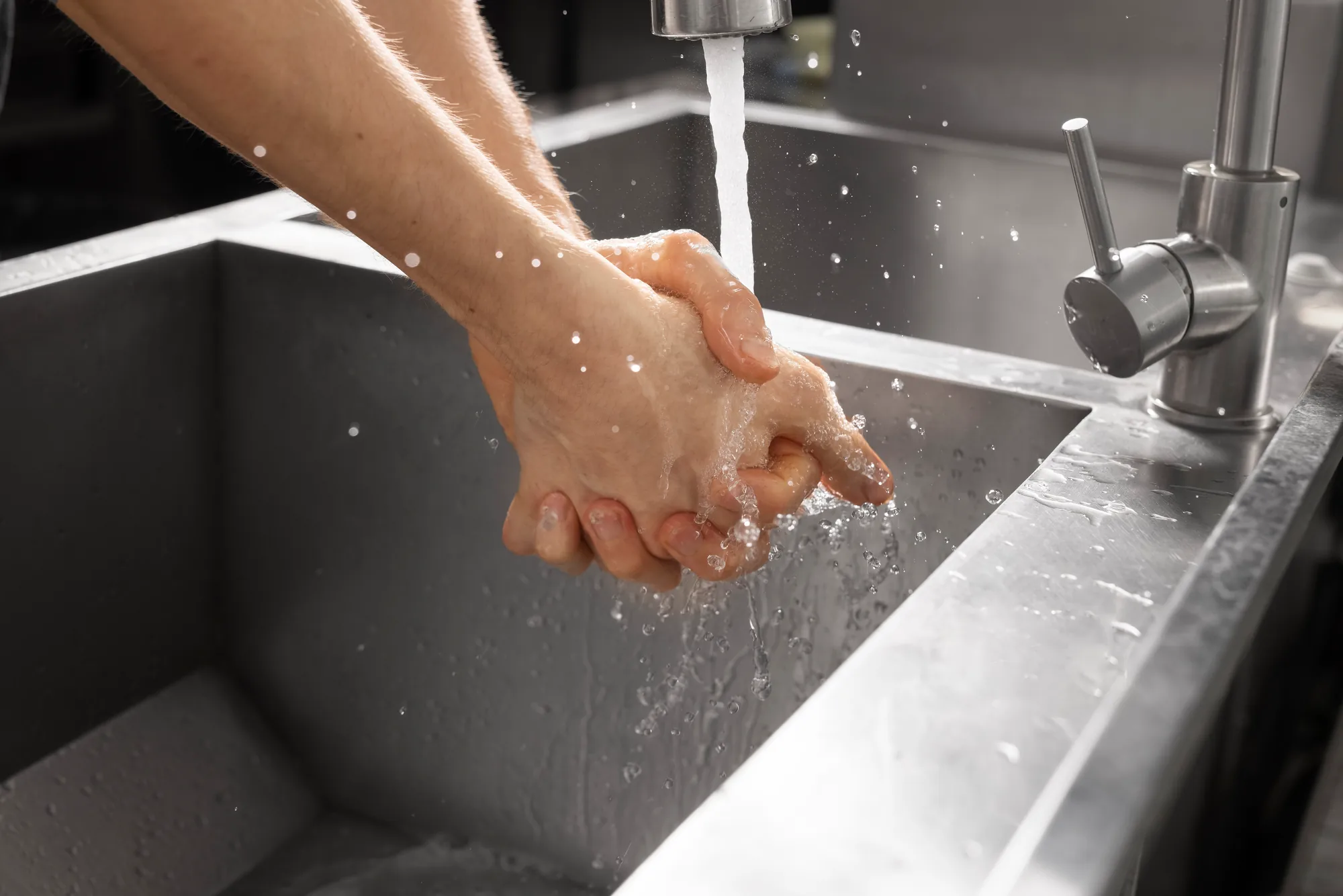 Hands rinsed under a tap at a steel sink