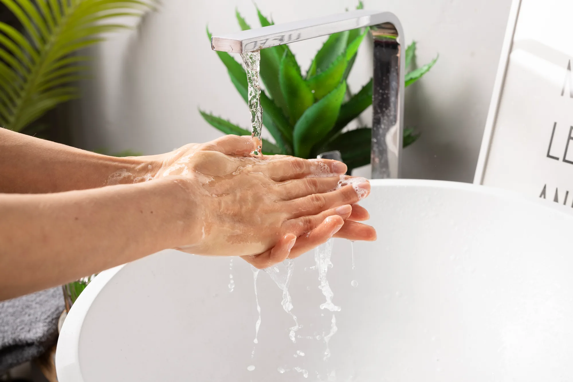 Hands under a running tap over a white basin