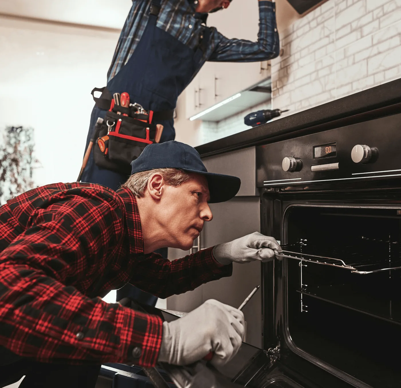 A plumber in a red checked shirt fitting a kitchen oven