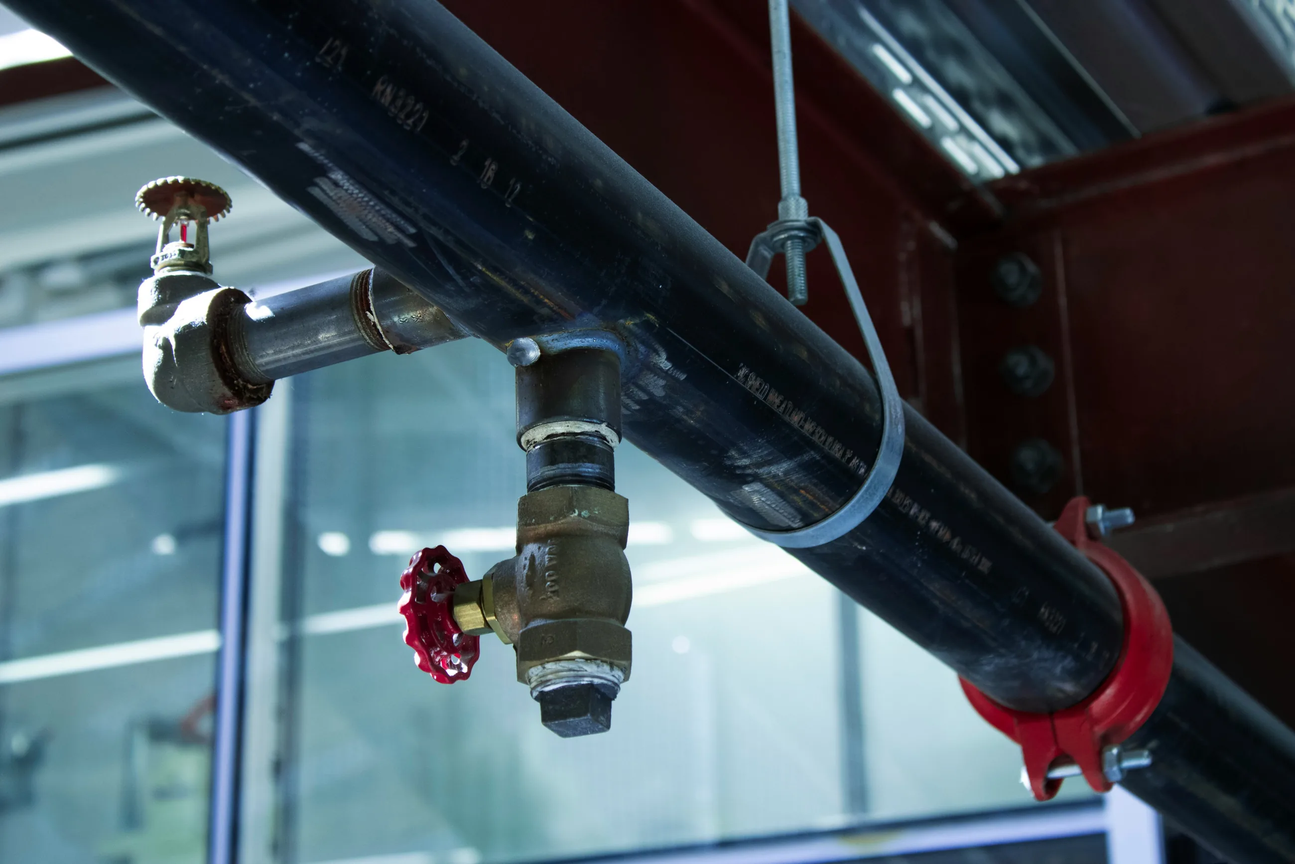A red valve on an overhead pipe in a commercial building