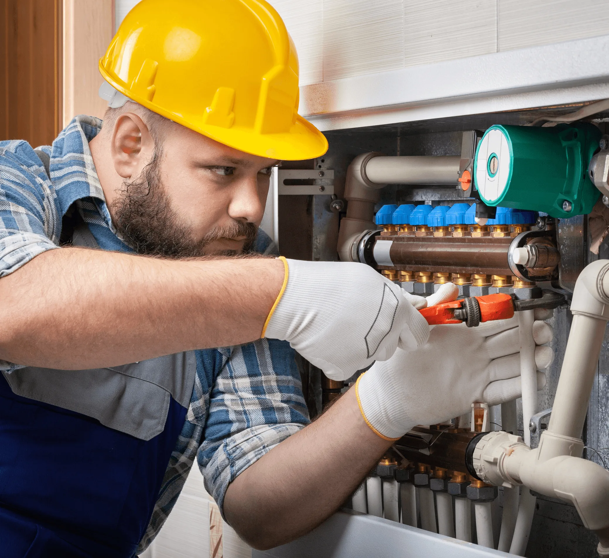 A plumber in a yellow hard hat at a heating manifold