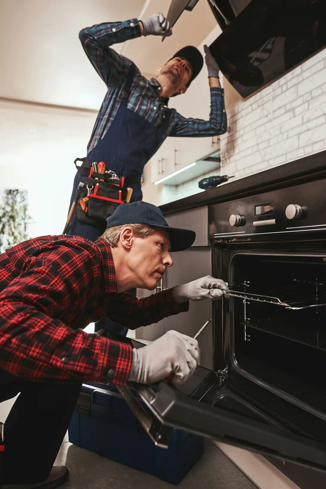 A plumber with a tool belt fitting a kitchen extractor