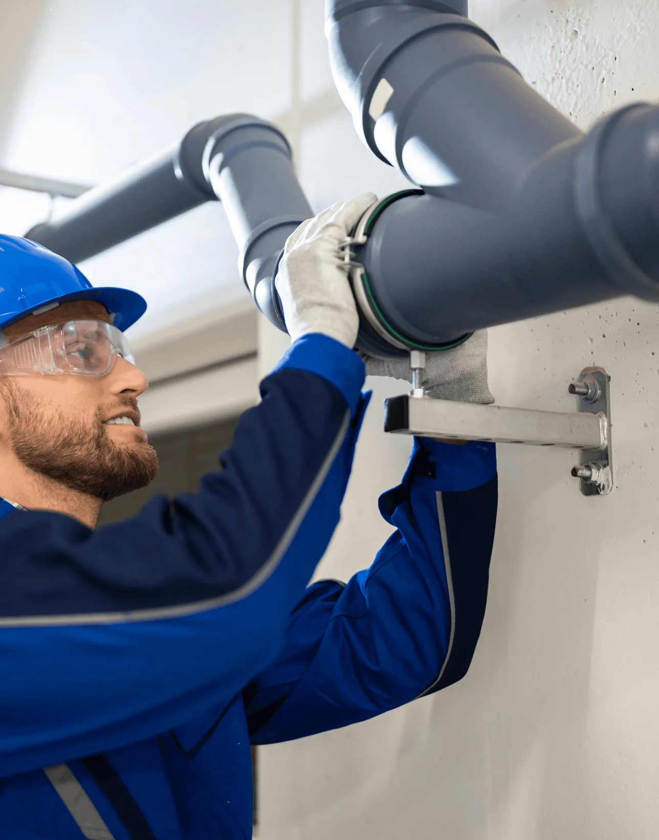 A plumber in safety glasses fitting a grey drain pipe