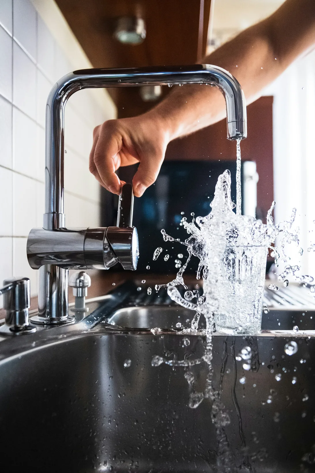 A hand turning a kitchen tap as water splashes