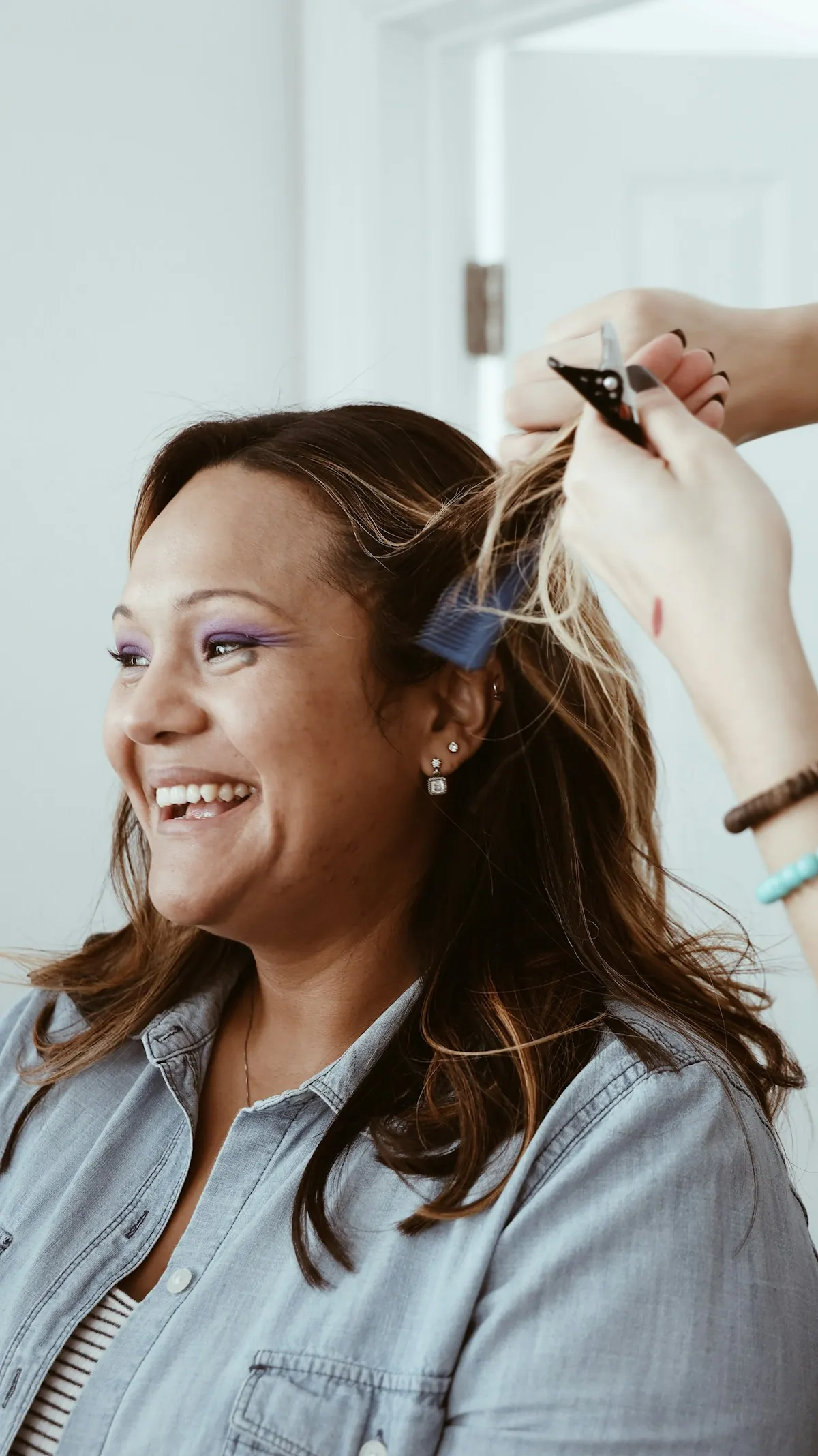 A smiling client having colour painted onto her hair in foils