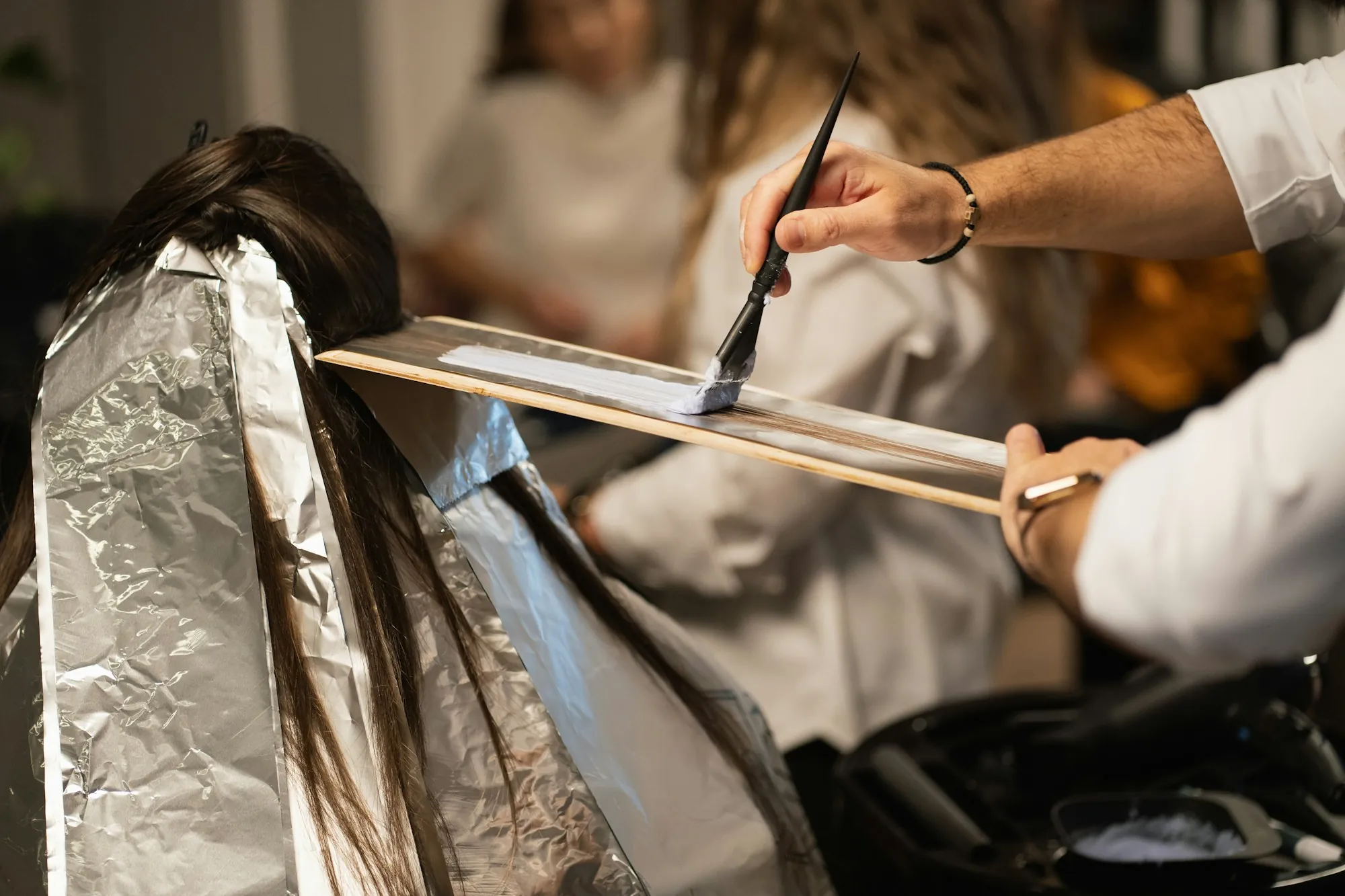 A colourist painting lightener onto a section of hair over a foil