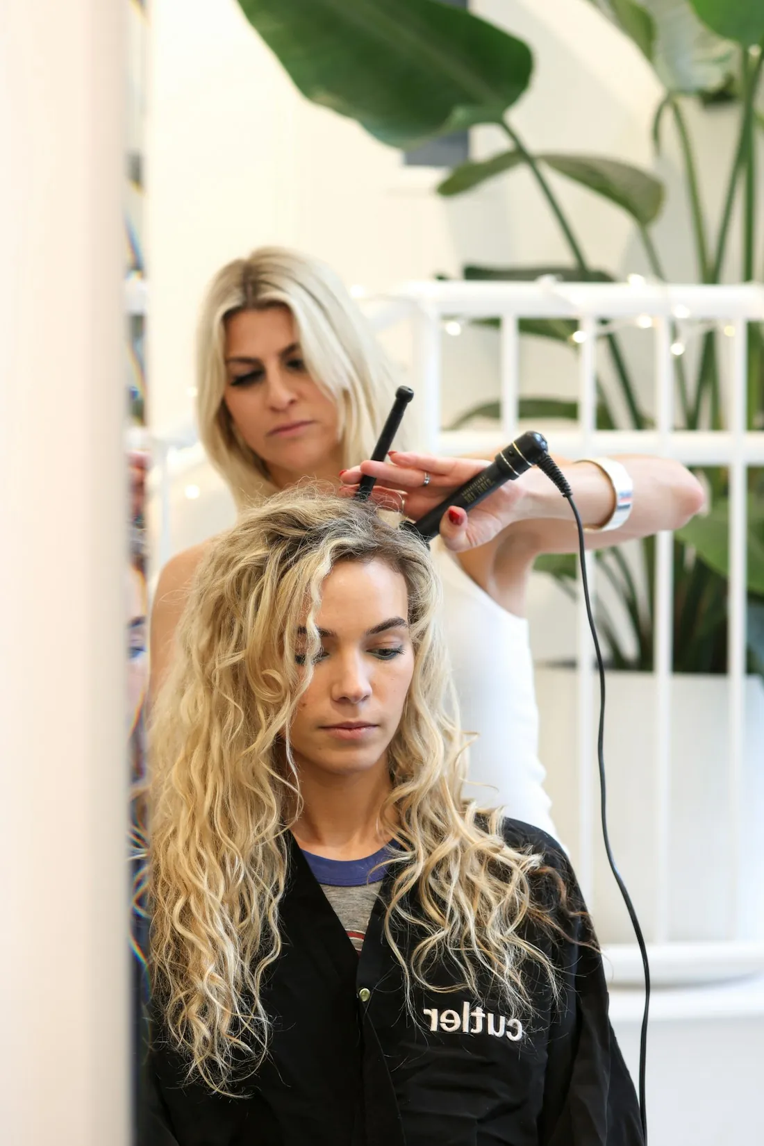A stylist setting loose curls in a client’s long blonde hair