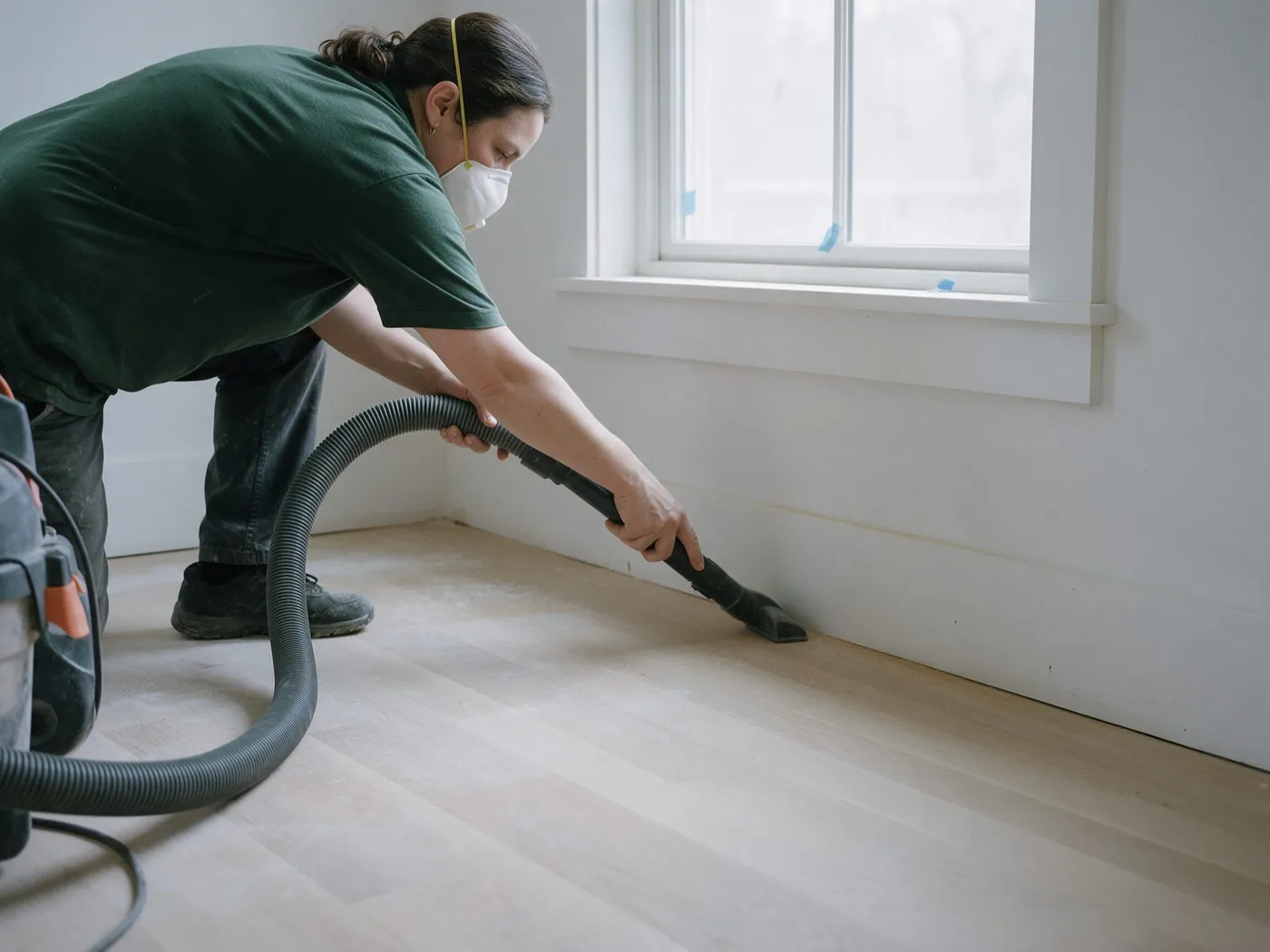Cleaner in a dust mask vacuuming a freshly finished floor