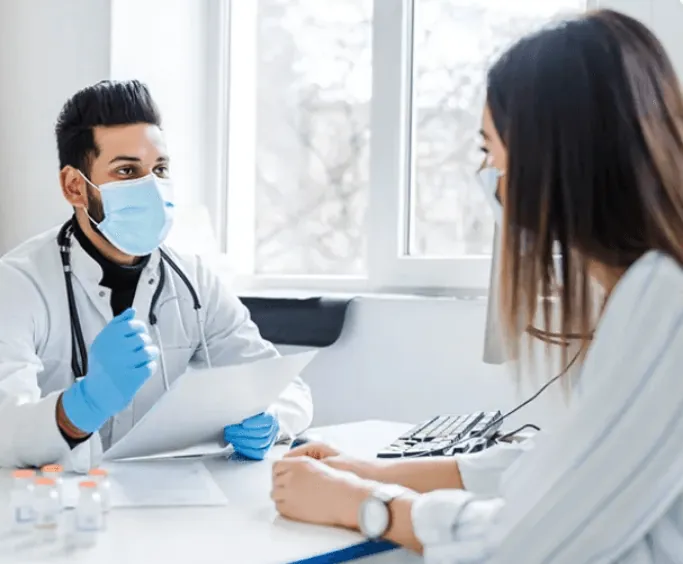 A dentist in a mask talking with a patient at a desk