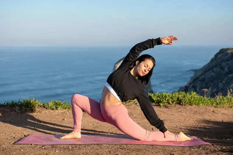 A woman in a side stretch on a mat by the sea