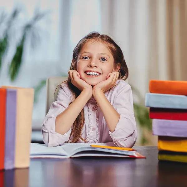A smiling girl resting her chin on her hands over a book