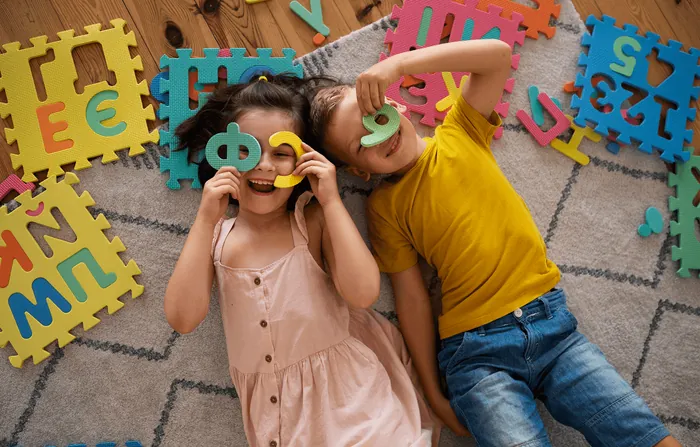 Children lying on a puzzle mat, peeking through cut-out letters
