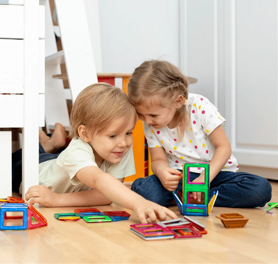 Two children building with colourful tiles on the floor