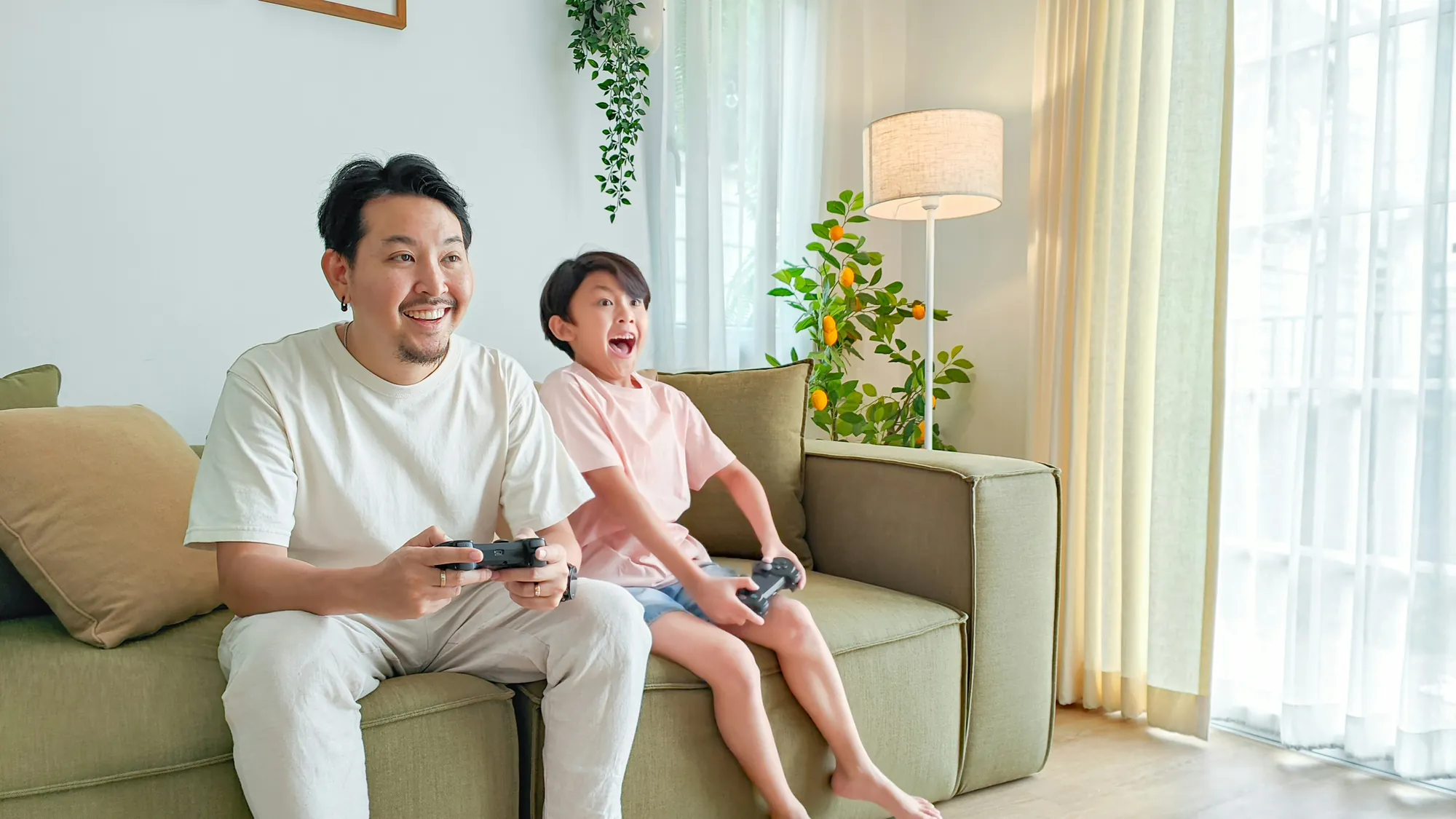 Father and son laughing on a sofa while playing video games