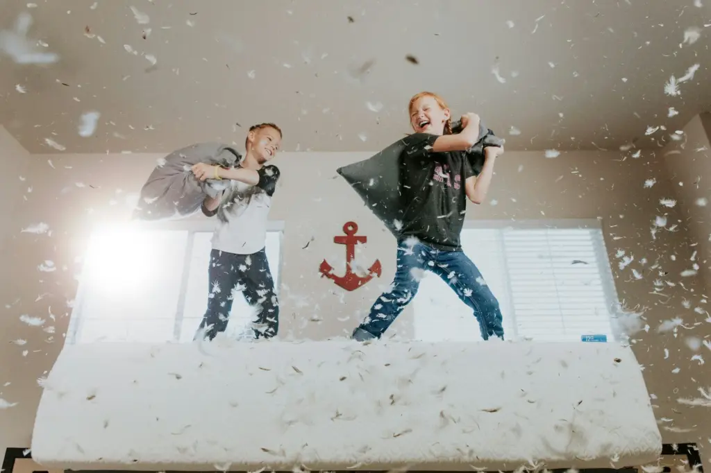Two boys having a pillow fight on a bed as feathers fly