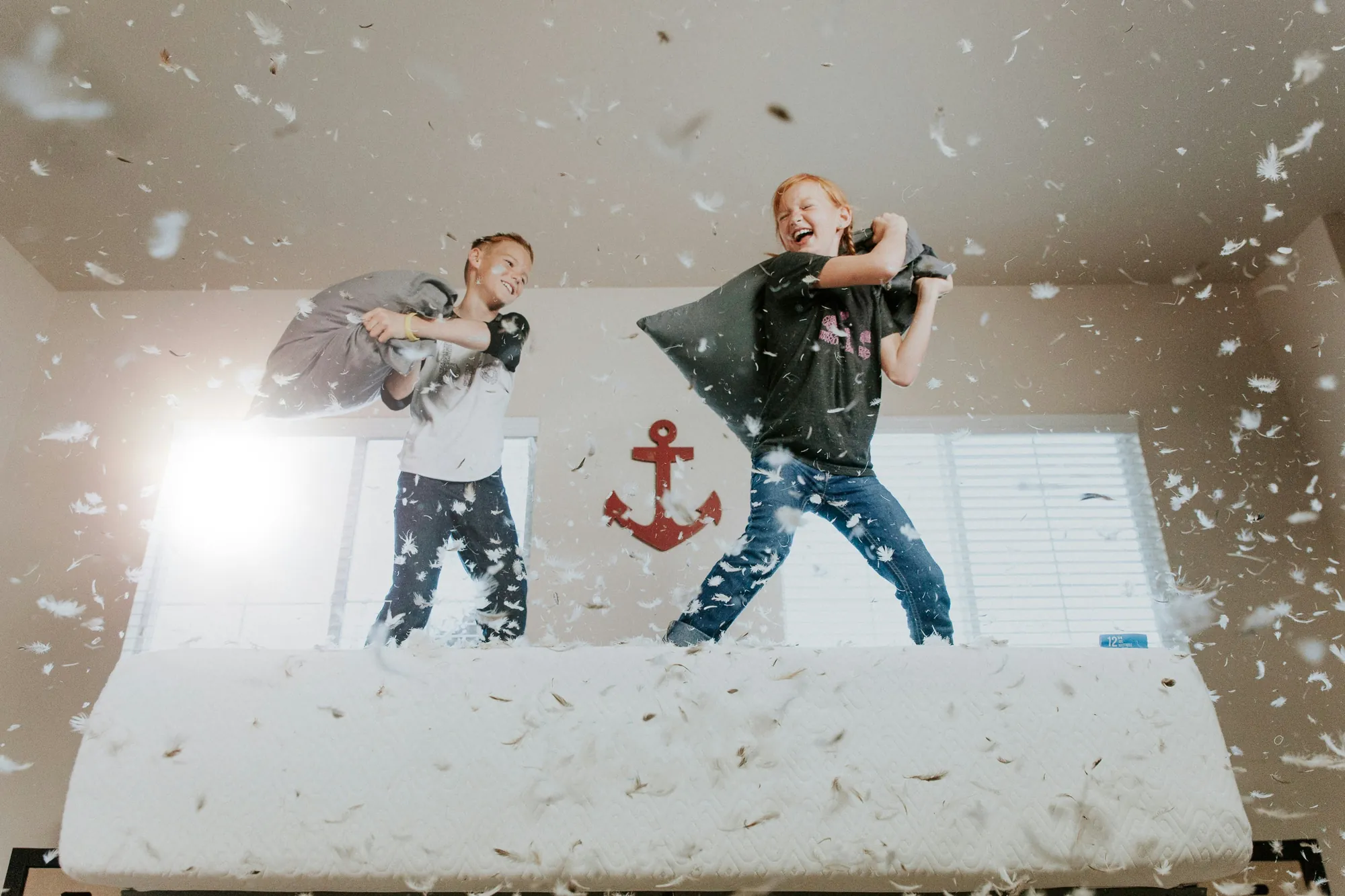 Two boys having a pillow fight on a bed as feathers fly