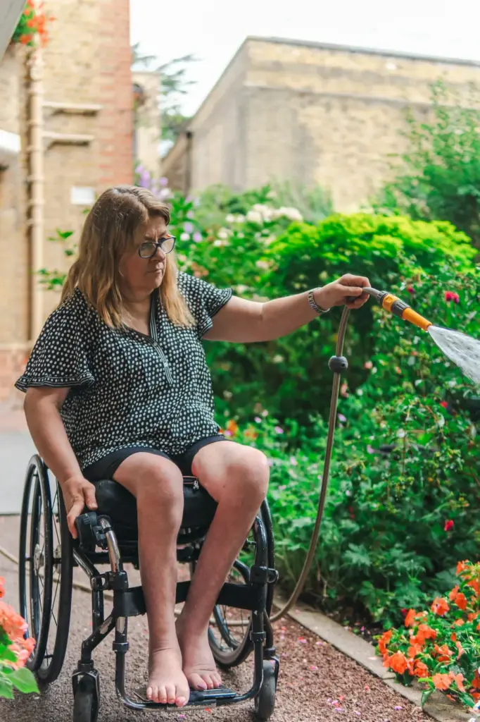 A gardener in a wheelchair watering the borders