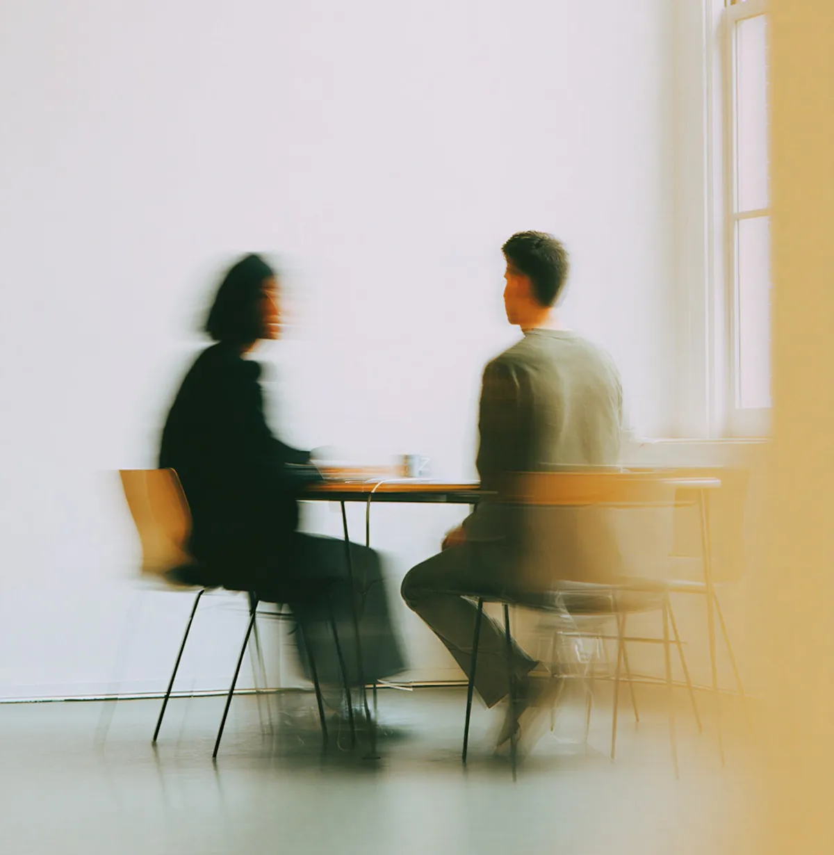 Two people talking at a table in a bright room