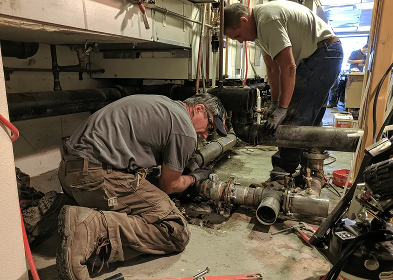 A plumber repairing large drain pipes in a commercial building