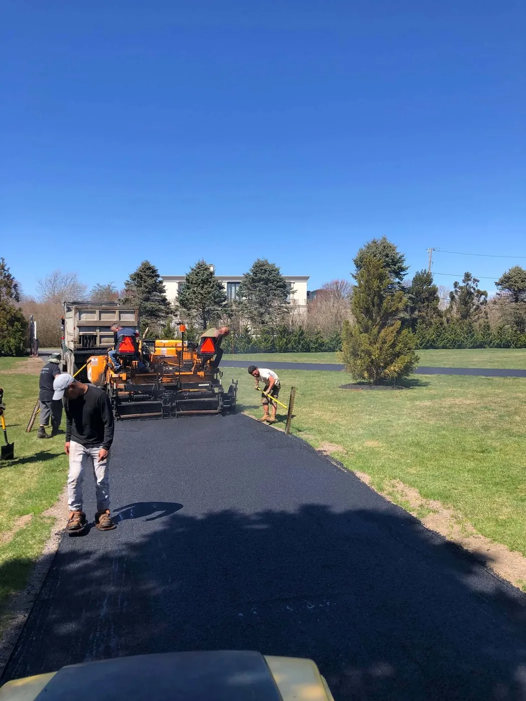 A paving crew laying a fresh asphalt driveway with a paver and a dump truck