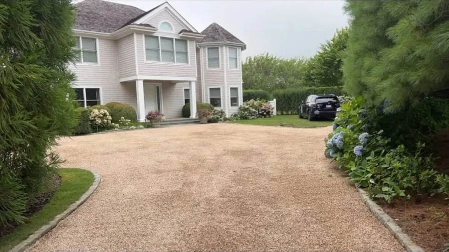 A finished pea gravel driveway leading to a white two-story house framed by landscaping
