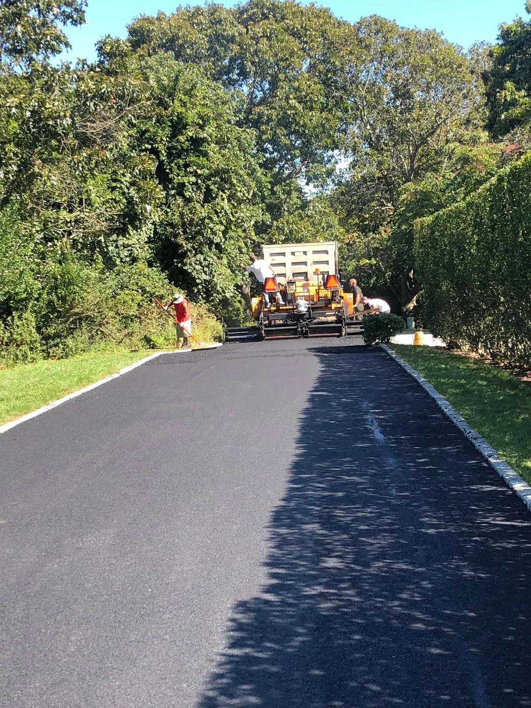 A long private road being resurfaced beside a granite curb and a hedgerow