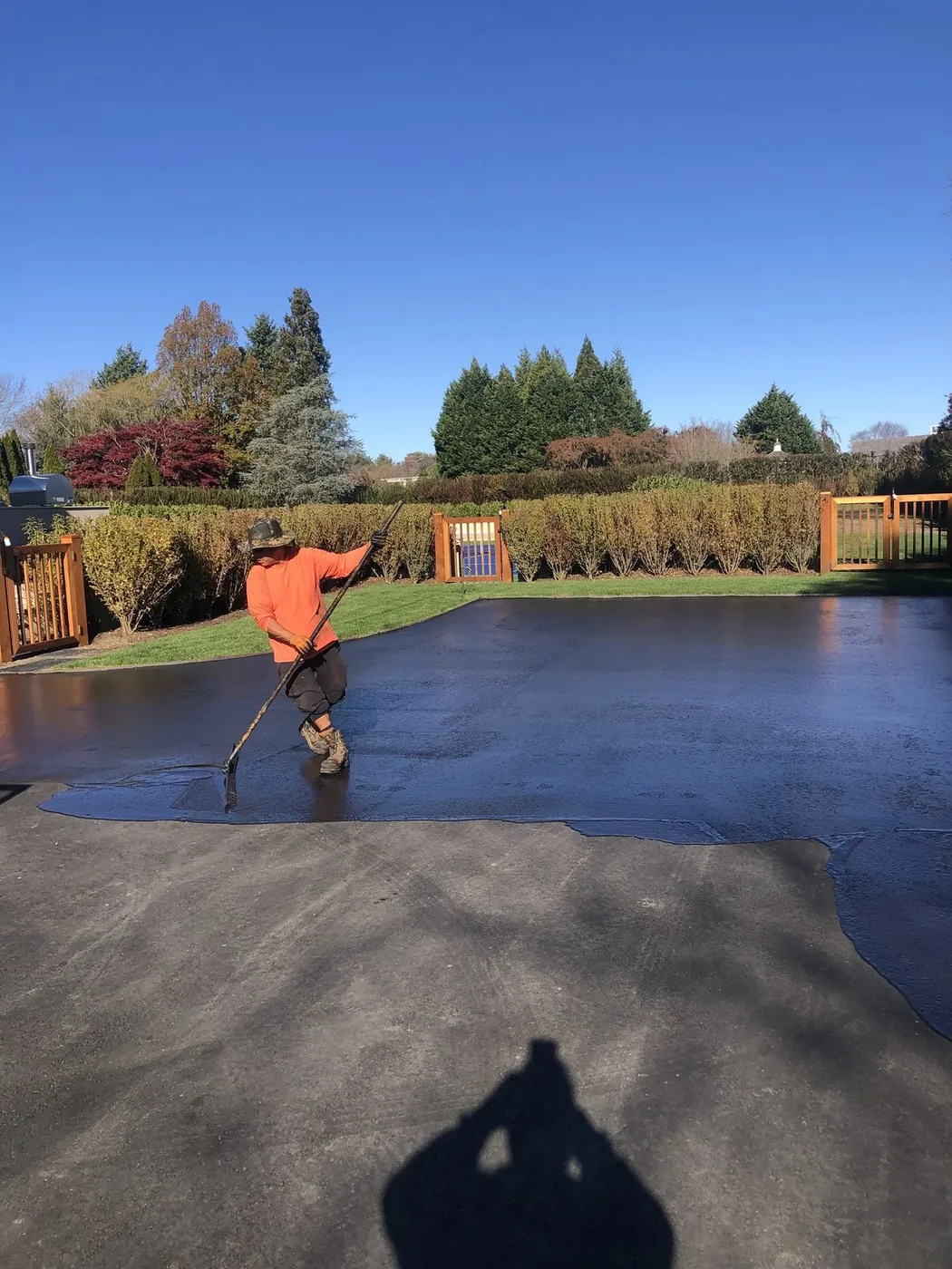 A worker spreading sealcoat across a driveway with a squeegee