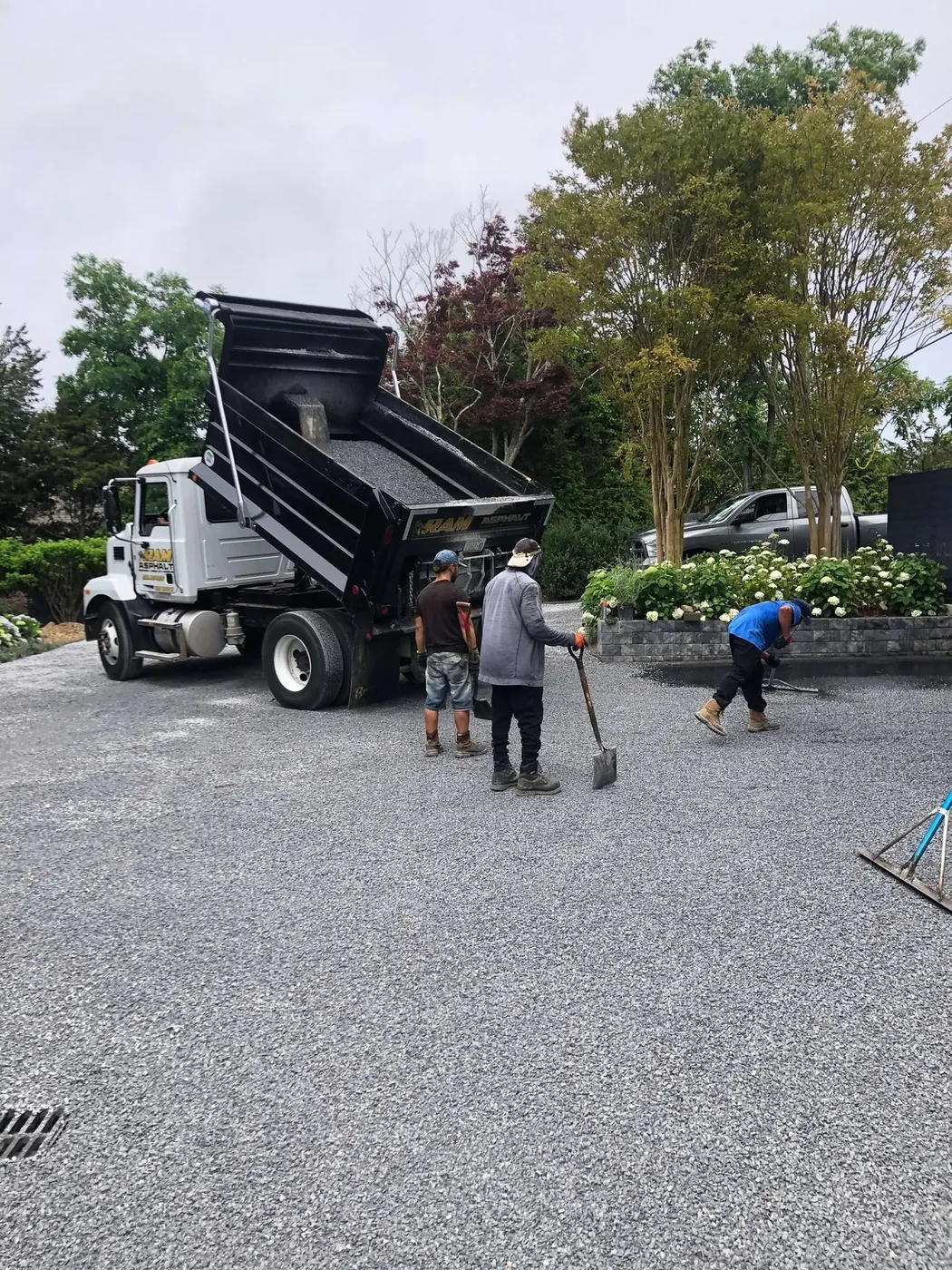 A dump truck spreading crushed stone while the crew rakes a new gravel driveway