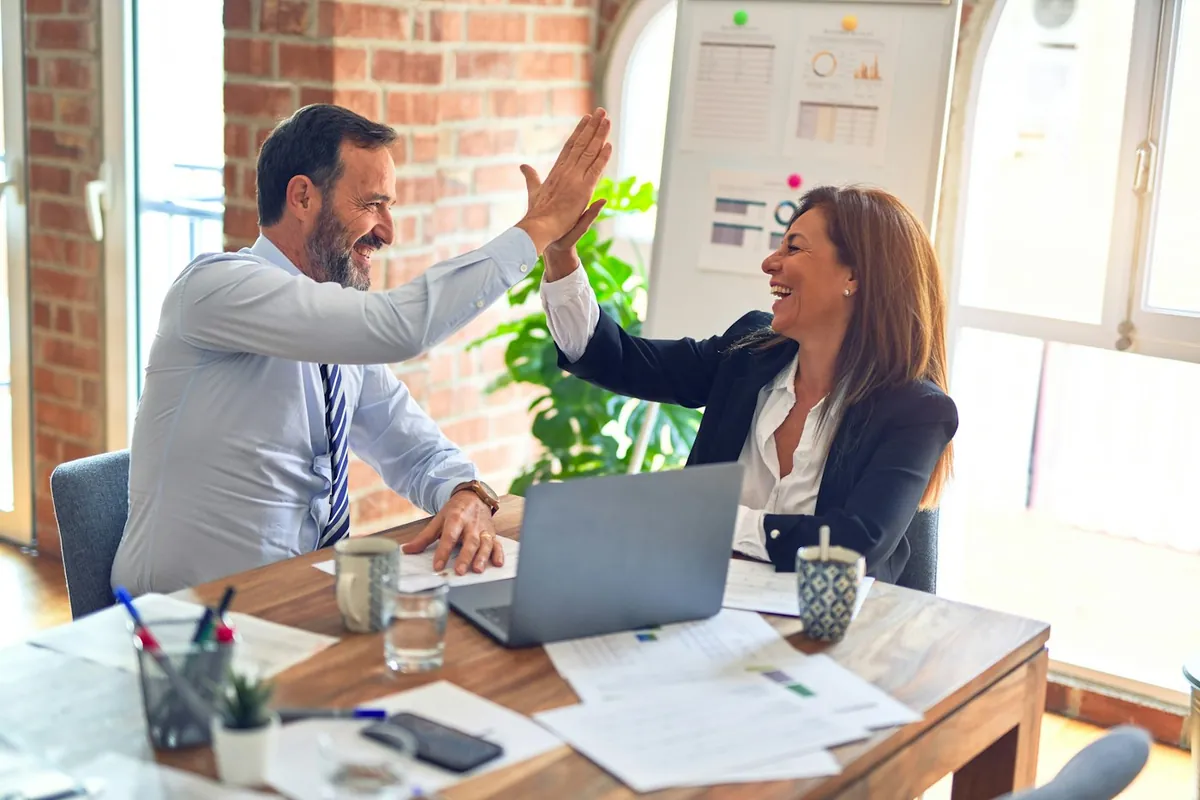 Two colleagues giving each other a high five at their desk
