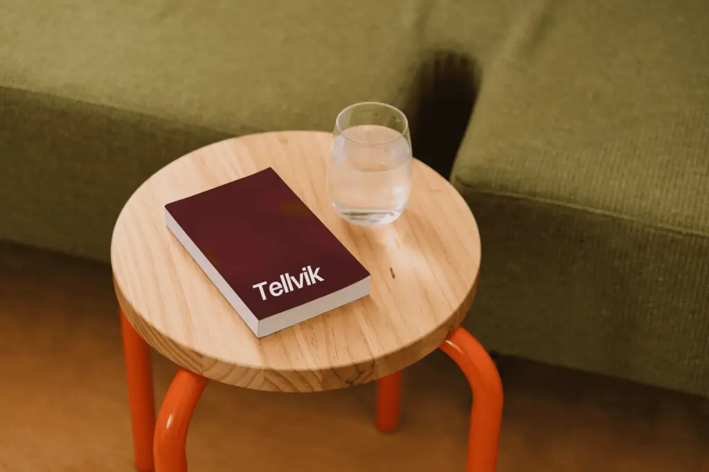 A red Tellvik book and a glass of water on a wooden stool