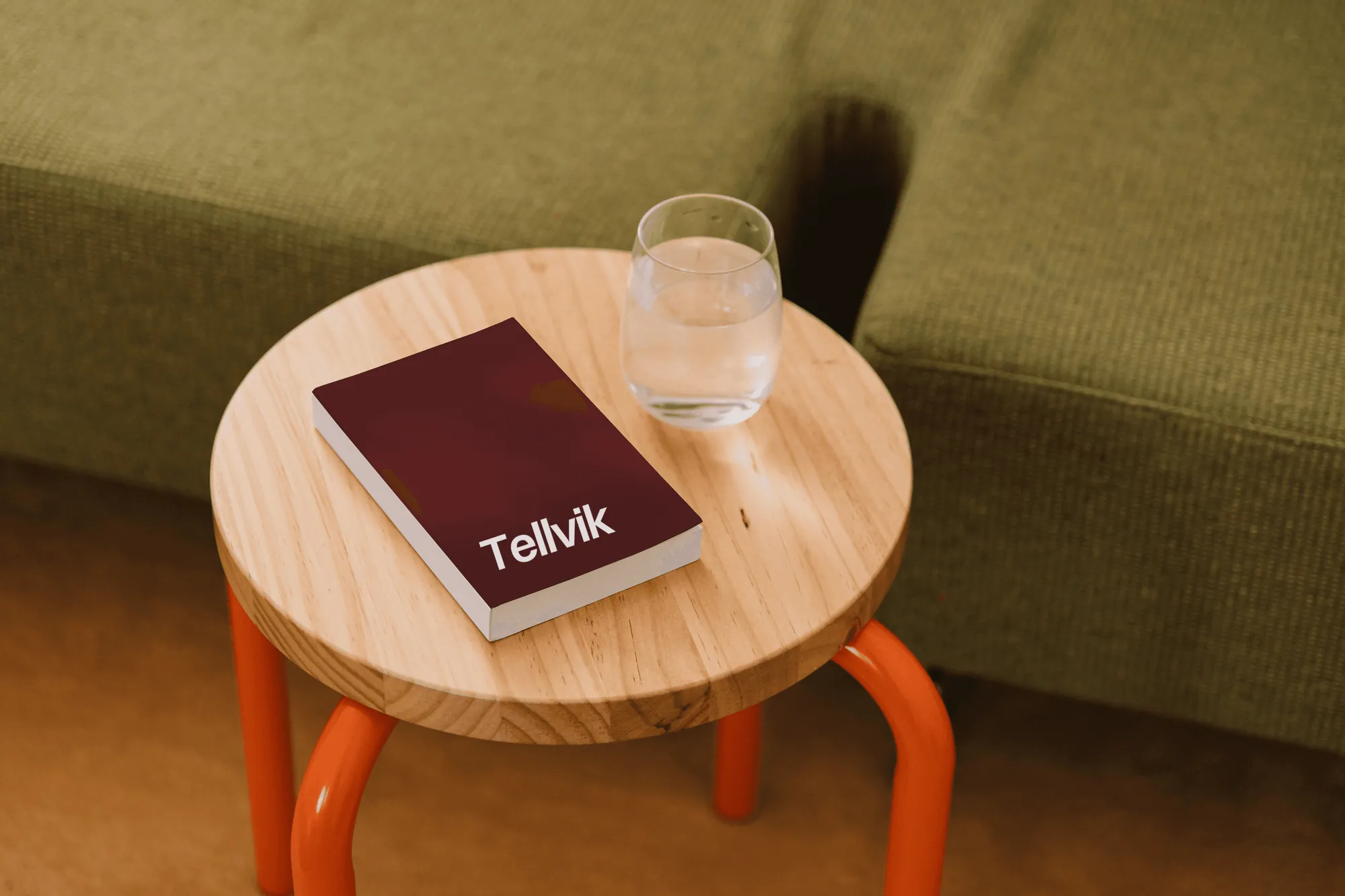 A red Tellvik book and a glass of water on a wooden stool