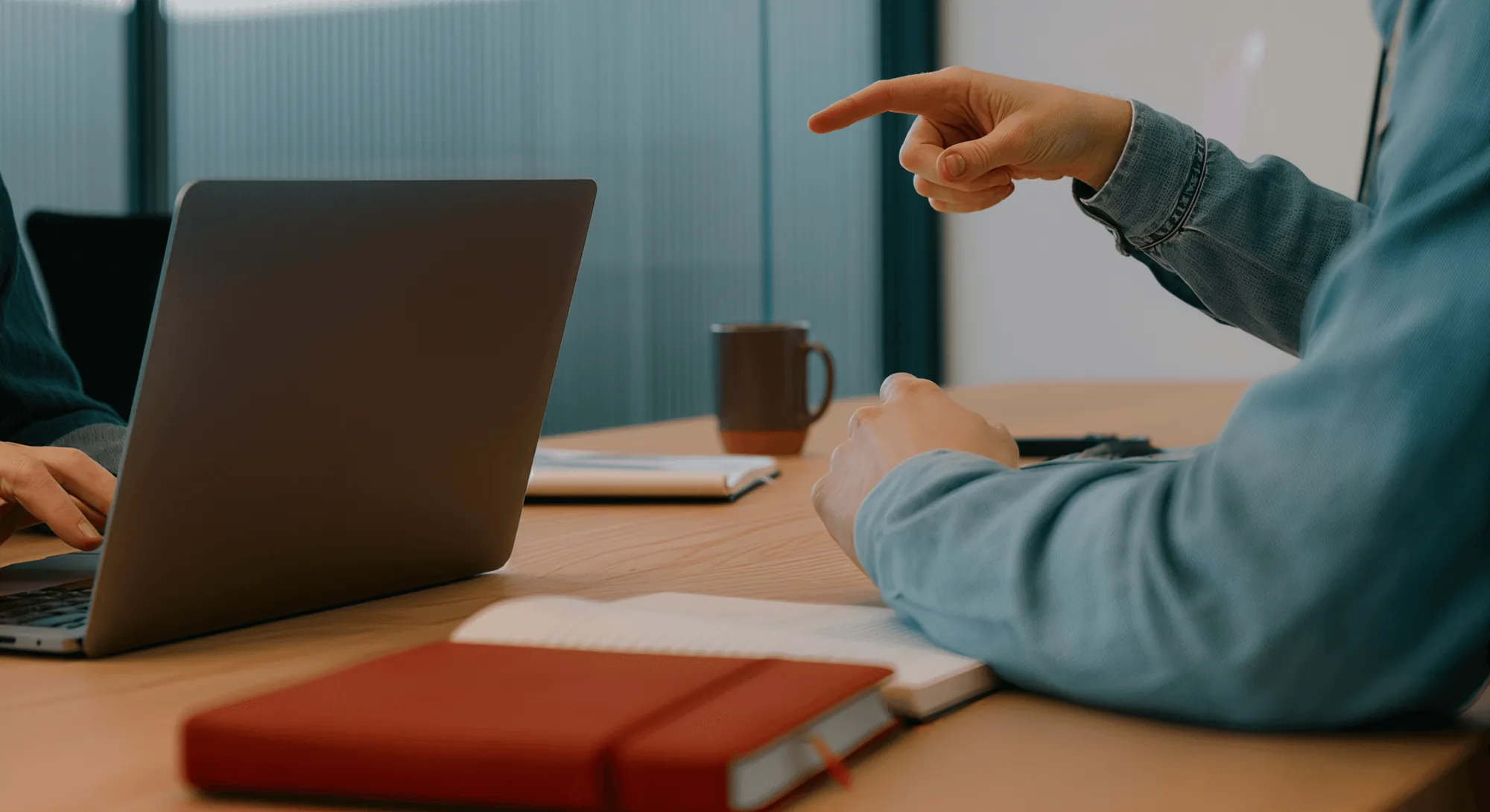 A hand pointing at a laptop screen beside a red notebook