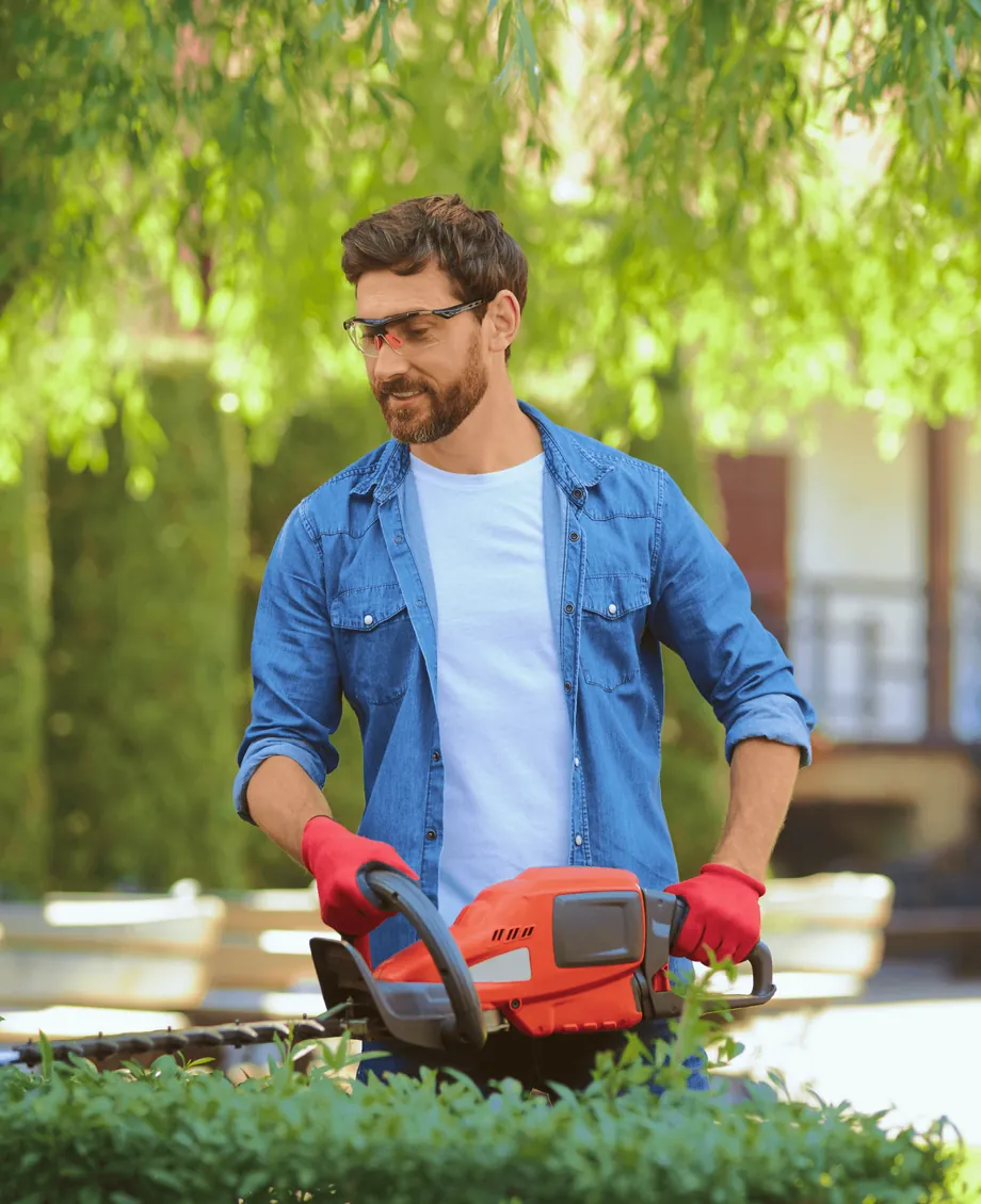 A gardener trimming a hedge with an electric trimmer