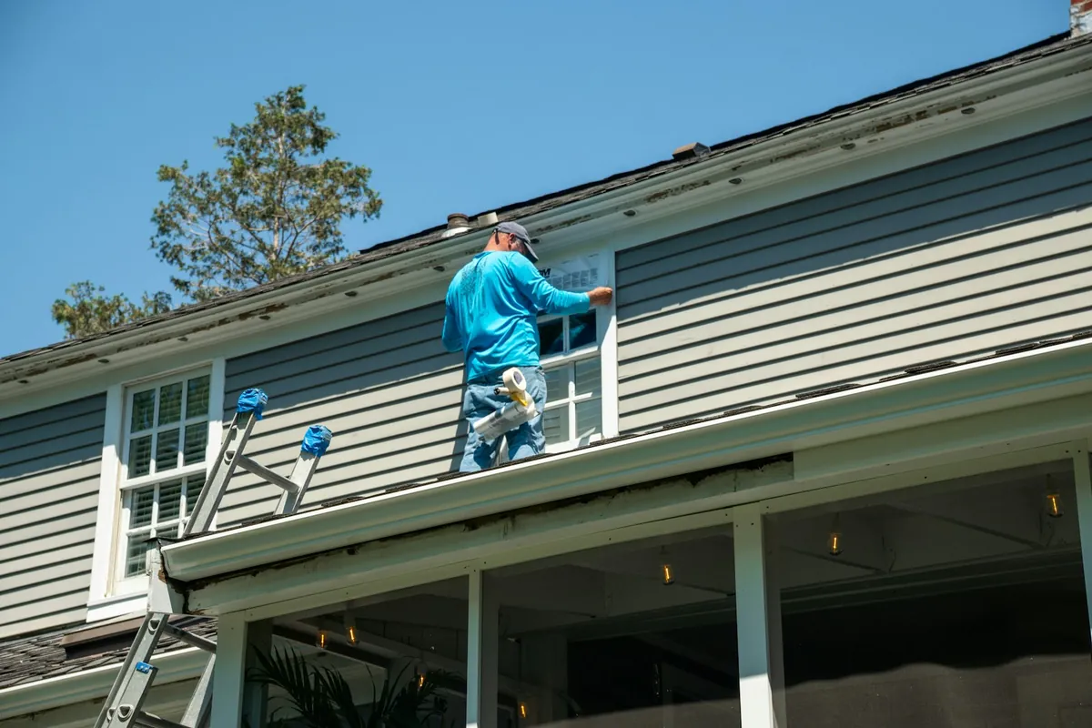 A technician washing the siding of a house from a ladder