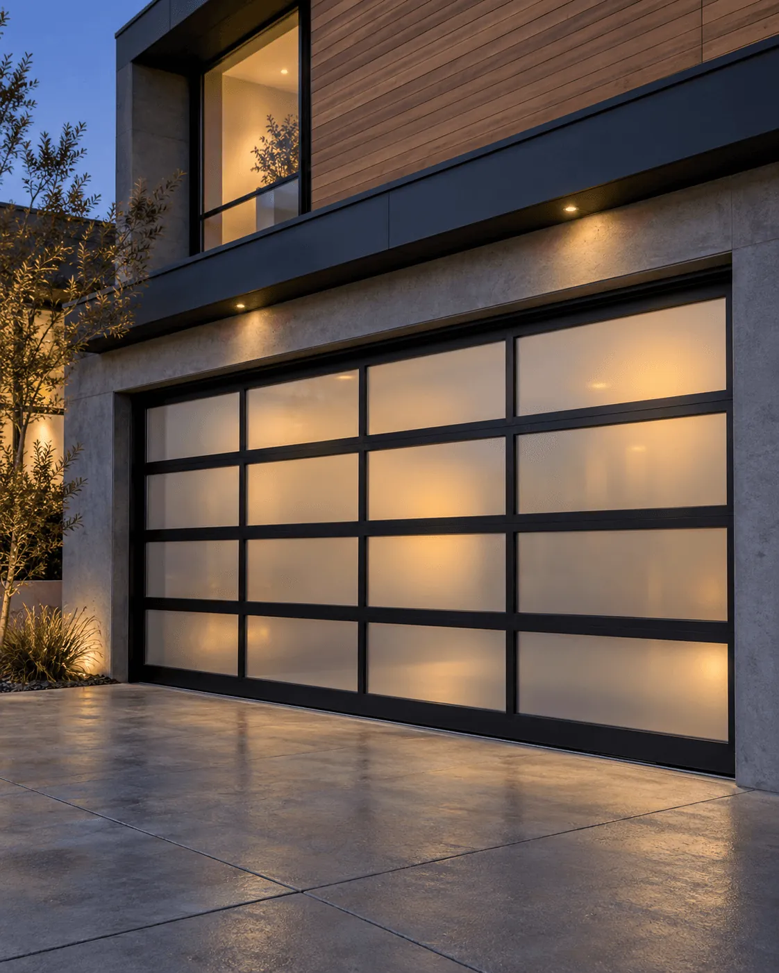 A full-view glass and aluminium garage door lit from inside at dusk