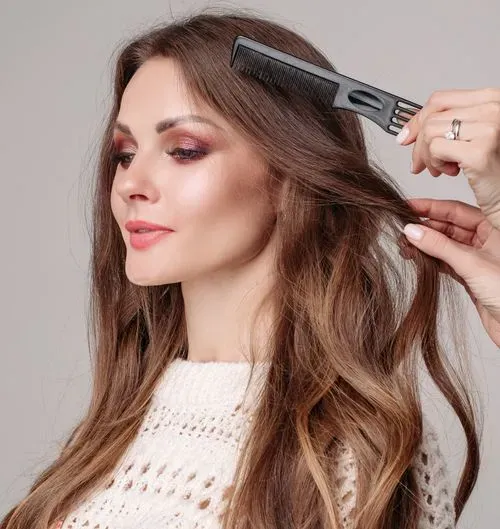 A stylist combing a client’s long wavy hair