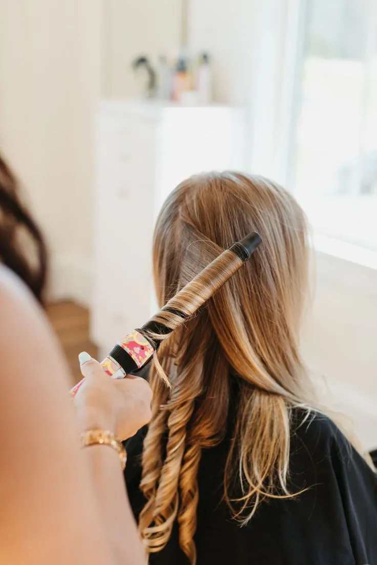A stylist curling long blonde hair with a curling iron