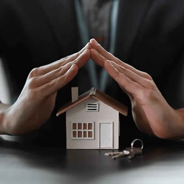 Hands sheltering a small model house