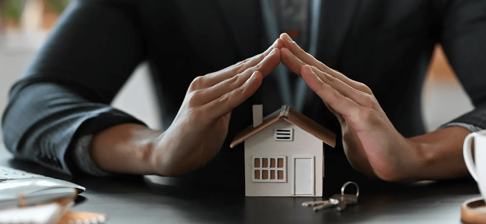 Hands sheltering a small model house