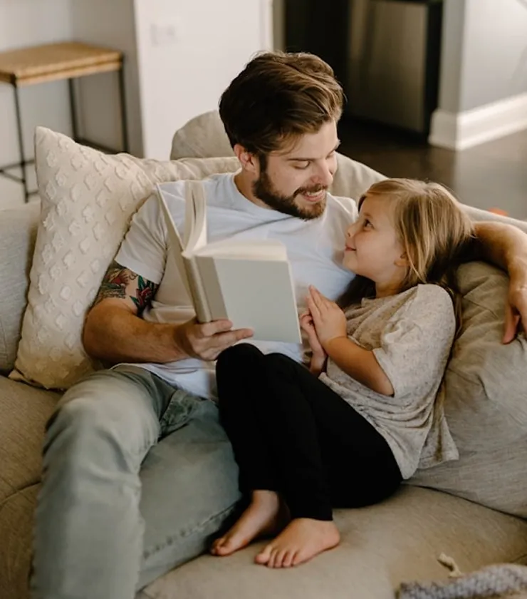 A father reading to his daughter on the sofa