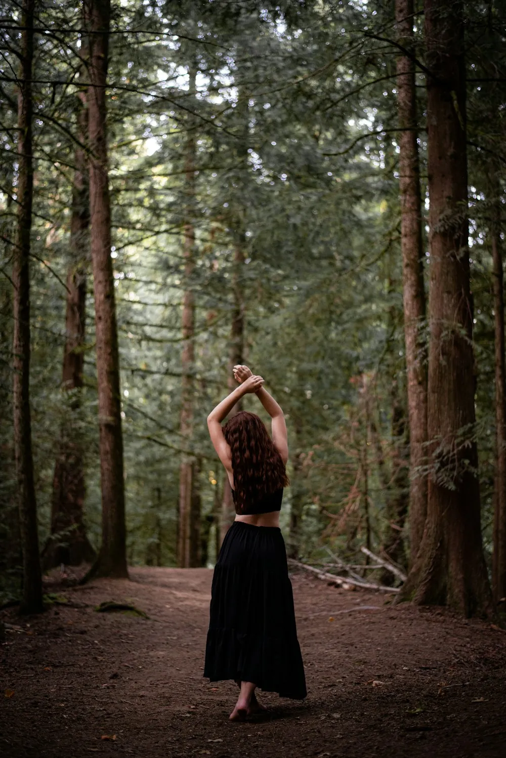 A woman stretching on a forest path among tall trees