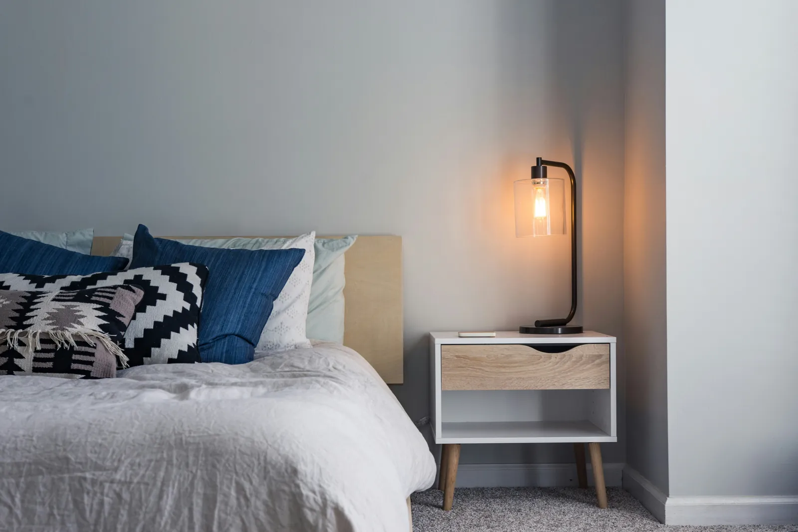 A bedside lamp glowing beside a made bed