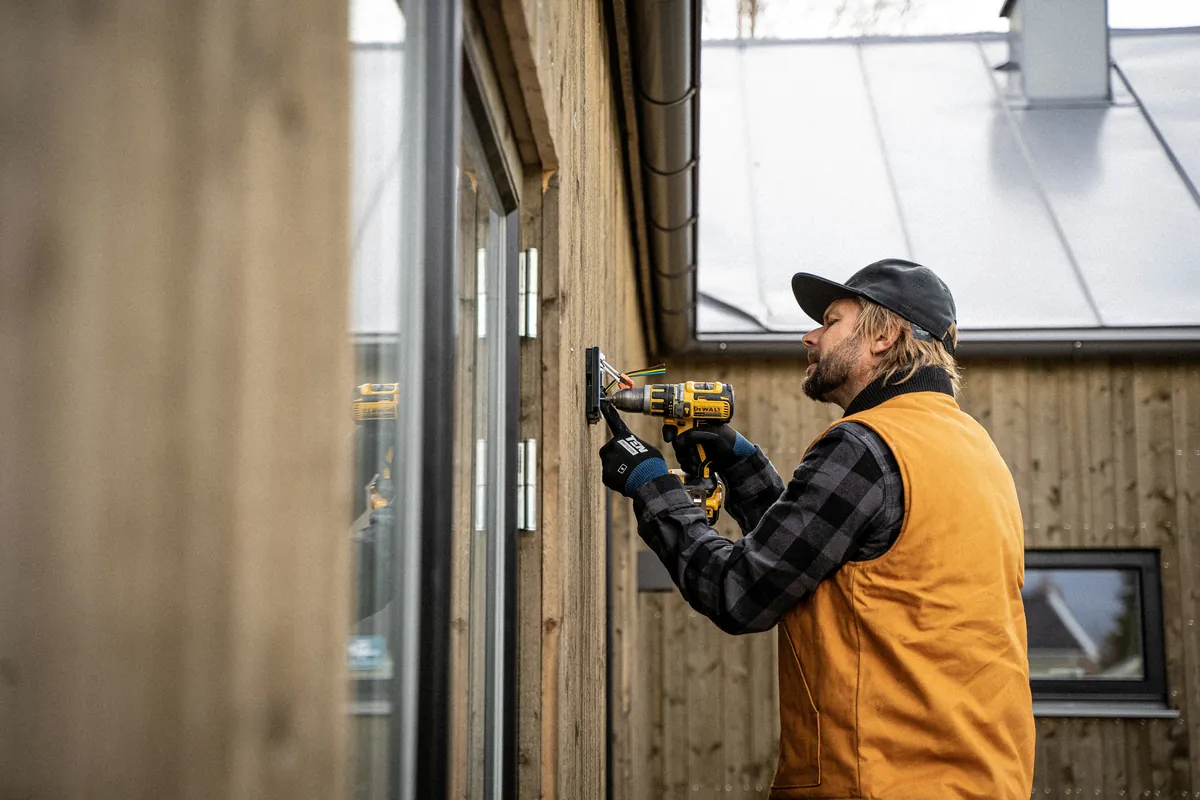 An electrician in a high-visibility vest drilling into a timber wall