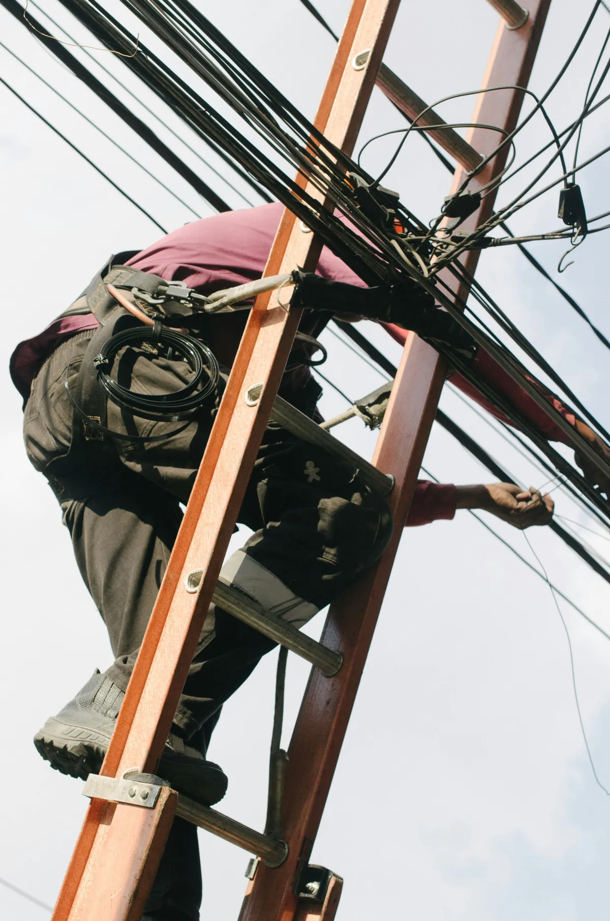 An electrician on a ladder working on overhead power lines